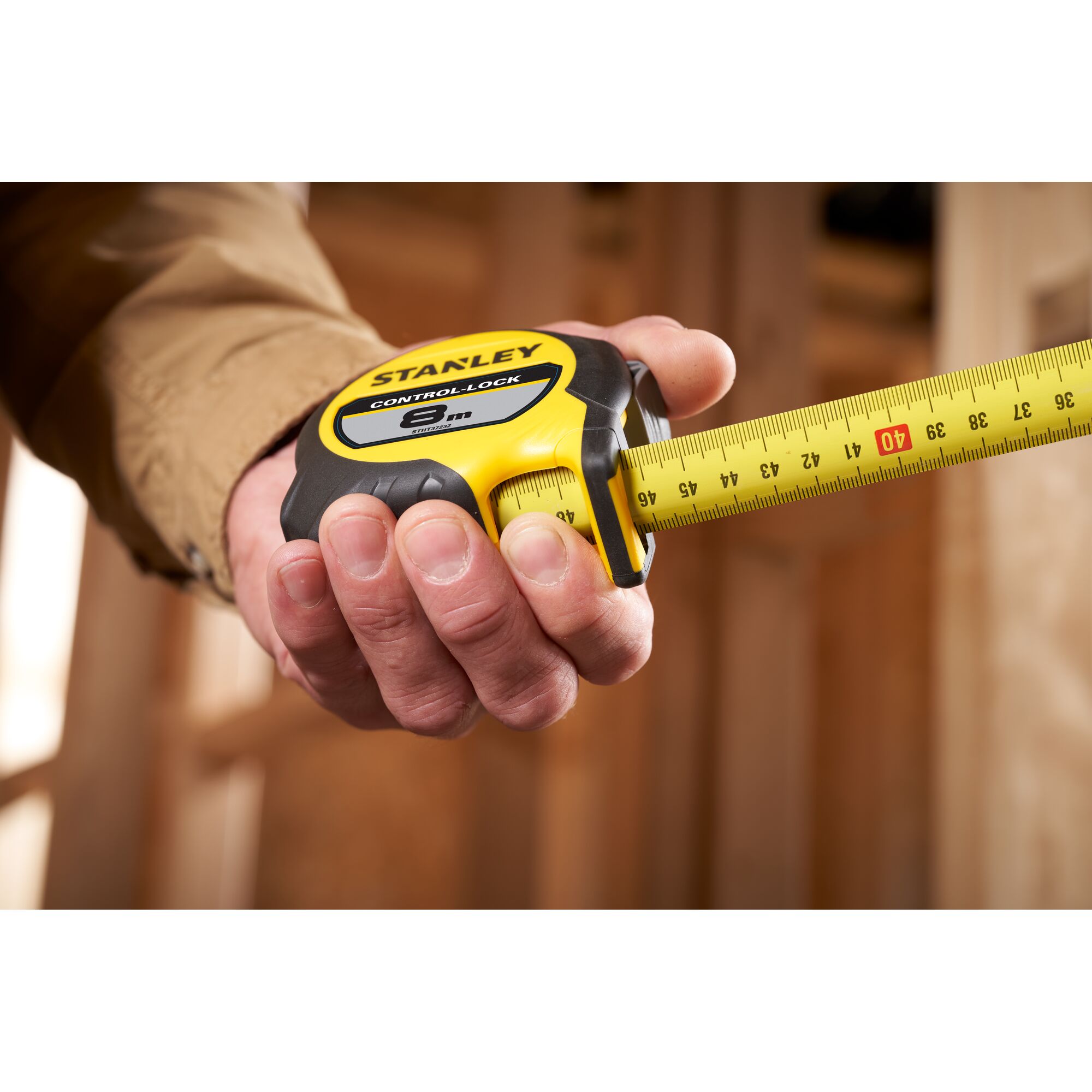 Photo of STANLEY STHT37232 tape measure with yellow and black casing, shown in use measuring wood.